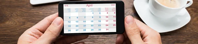Kalender auf einem Smartphone mit Kaffeetasse und Tastatur mit Maus im Hintergrund 